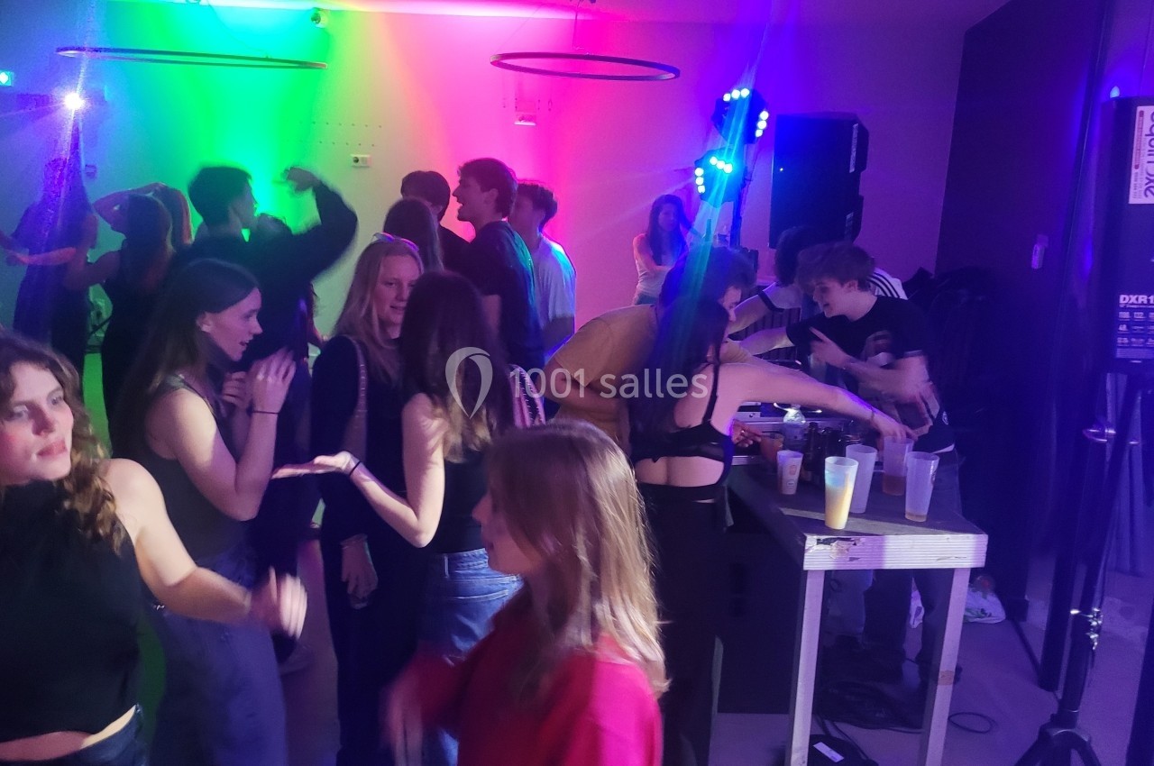 Des personnes dansent et discutent dans une ambiance festive avec éclairages colorés et musique en arrière-plan.