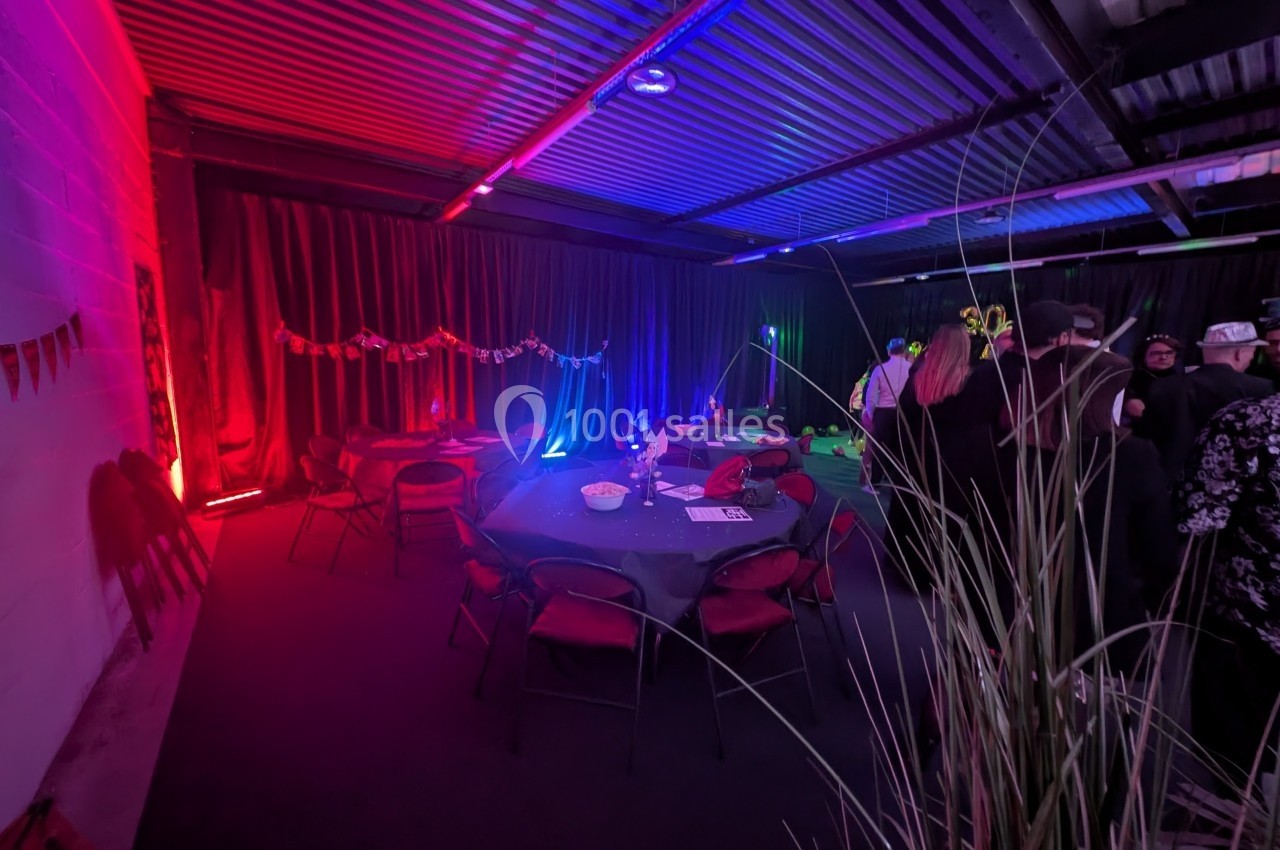 Salle décorée avec des guirlandes et éclairages colorés, tables rondes dressées, ambiance festive et tamisée.