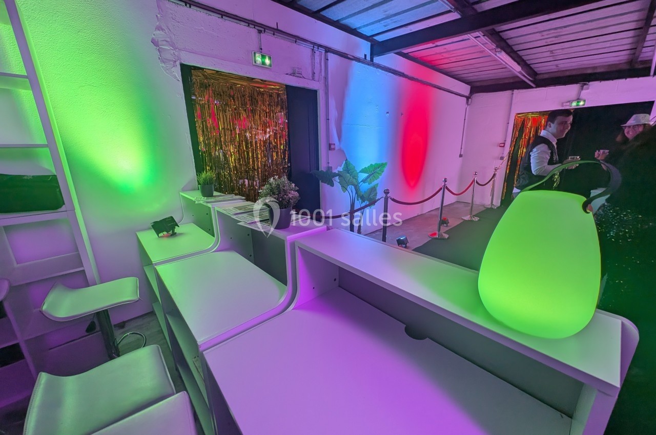 Comptoir blanc dans un espace décoré de lumières colorées, avec plantes et rideaux dorés en arrière-plan.