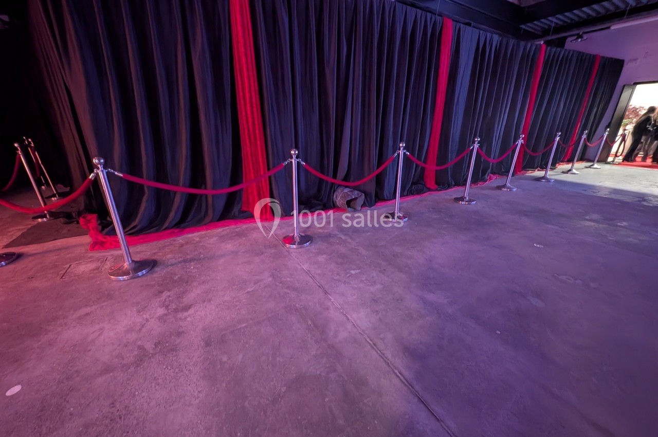 Rideaux noirs avec des bandes rouges, délimités par des poteaux et cordons rouges dans un espace intérieur.