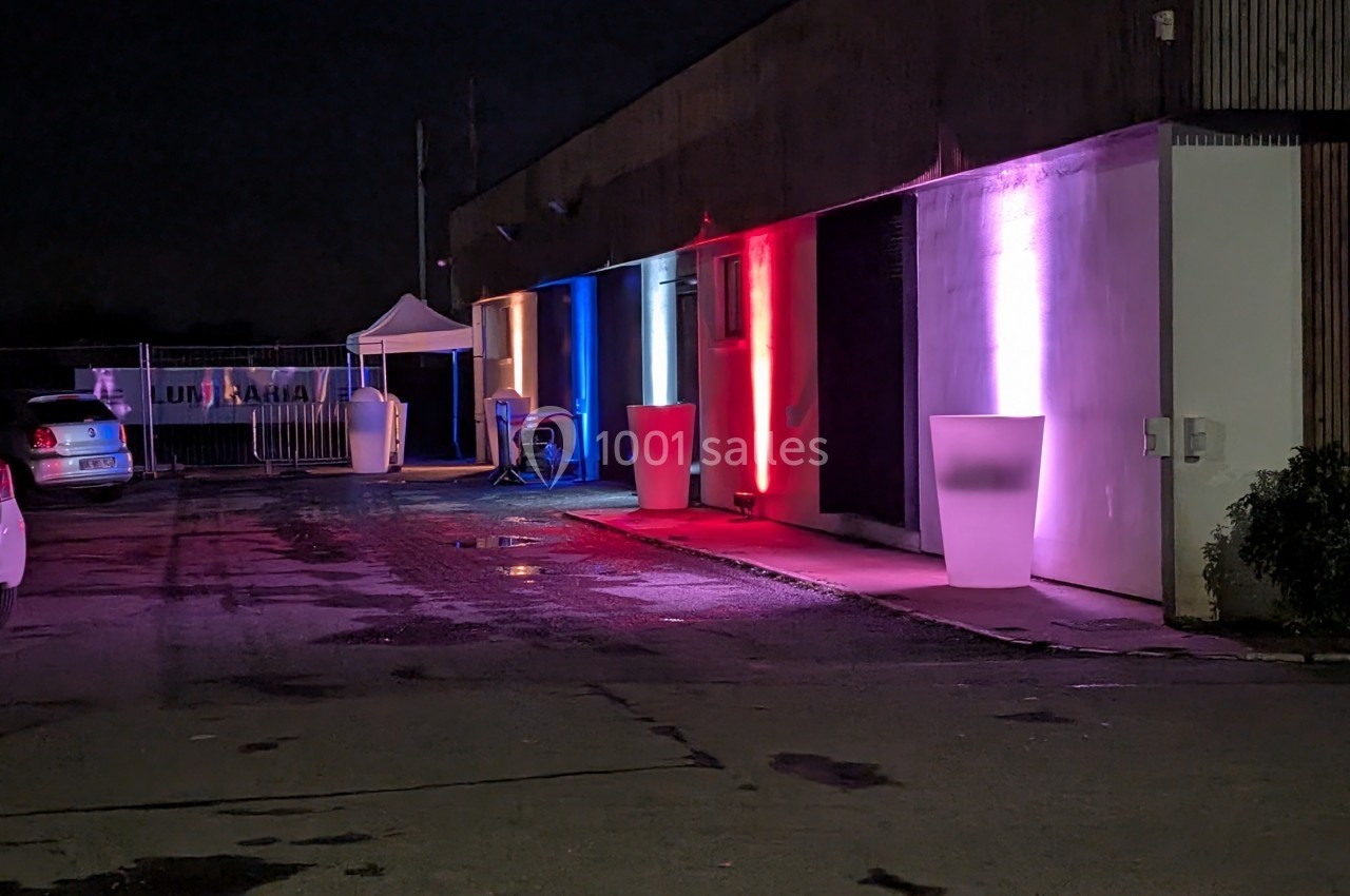 Façade d'un bâtiment éclairée par des lumières colorées rouge, bleue et blanche, avec des objets lumineux devant.