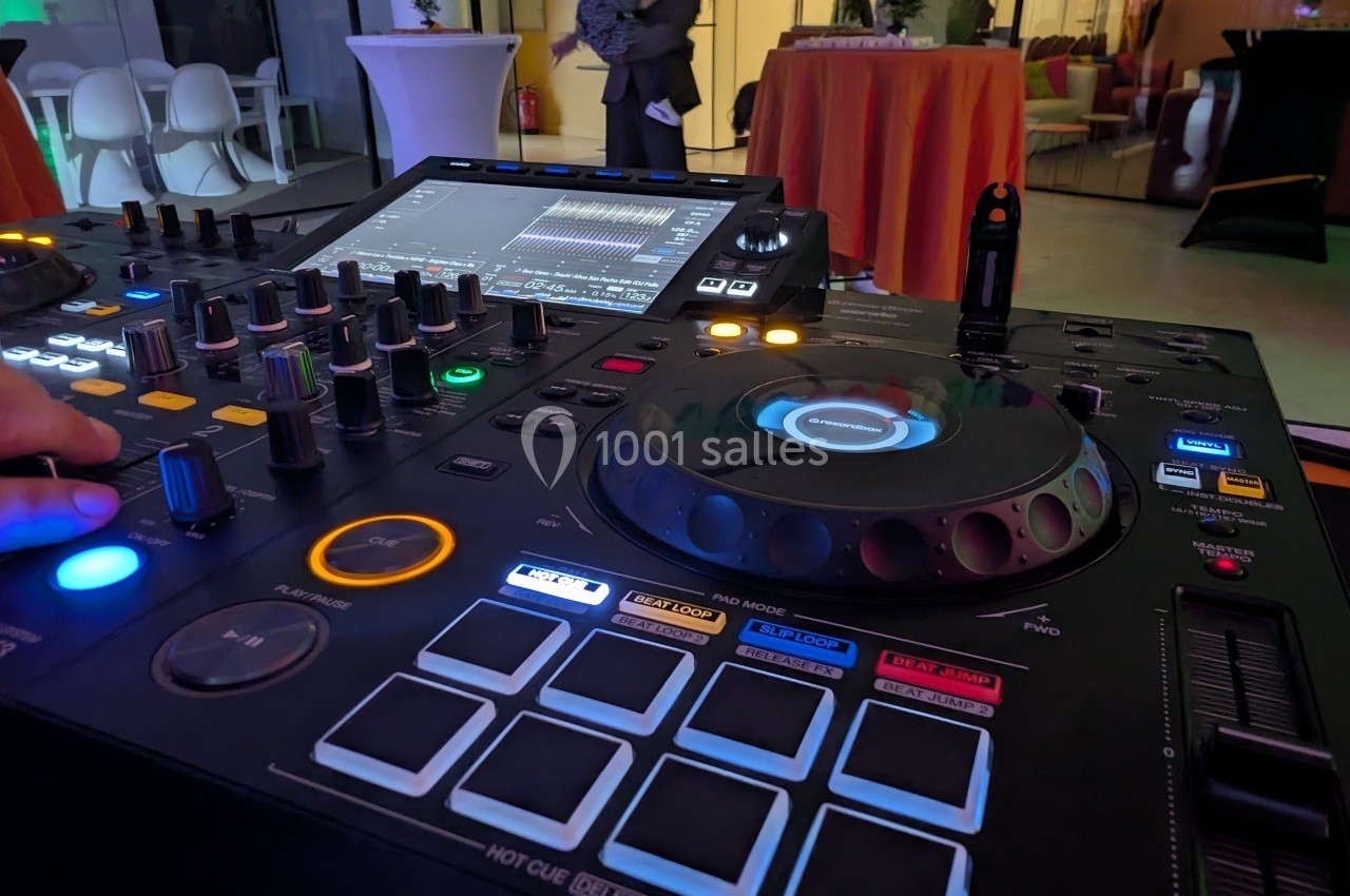 Console de mixage DJ avec boutons lumineux et écran tactile utilisée lors d'un événement en intérieur.