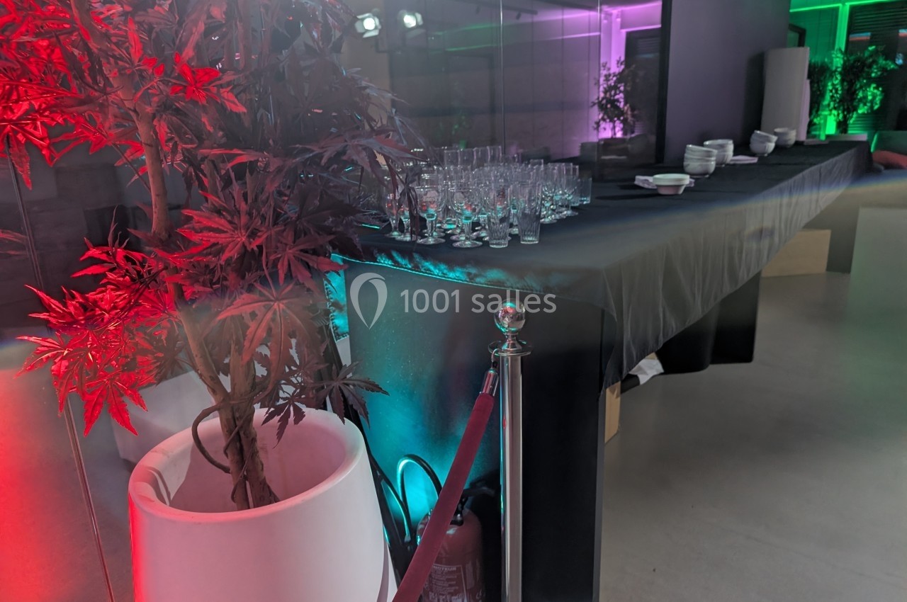 Table dressée avec des verres et des bols, éclairage coloré, plante en pot et extincteur au premier plan.