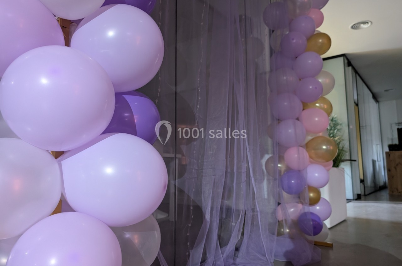 Guirlandes de ballons pastel et rideaux transparents décorant un espace intérieur lumineux.