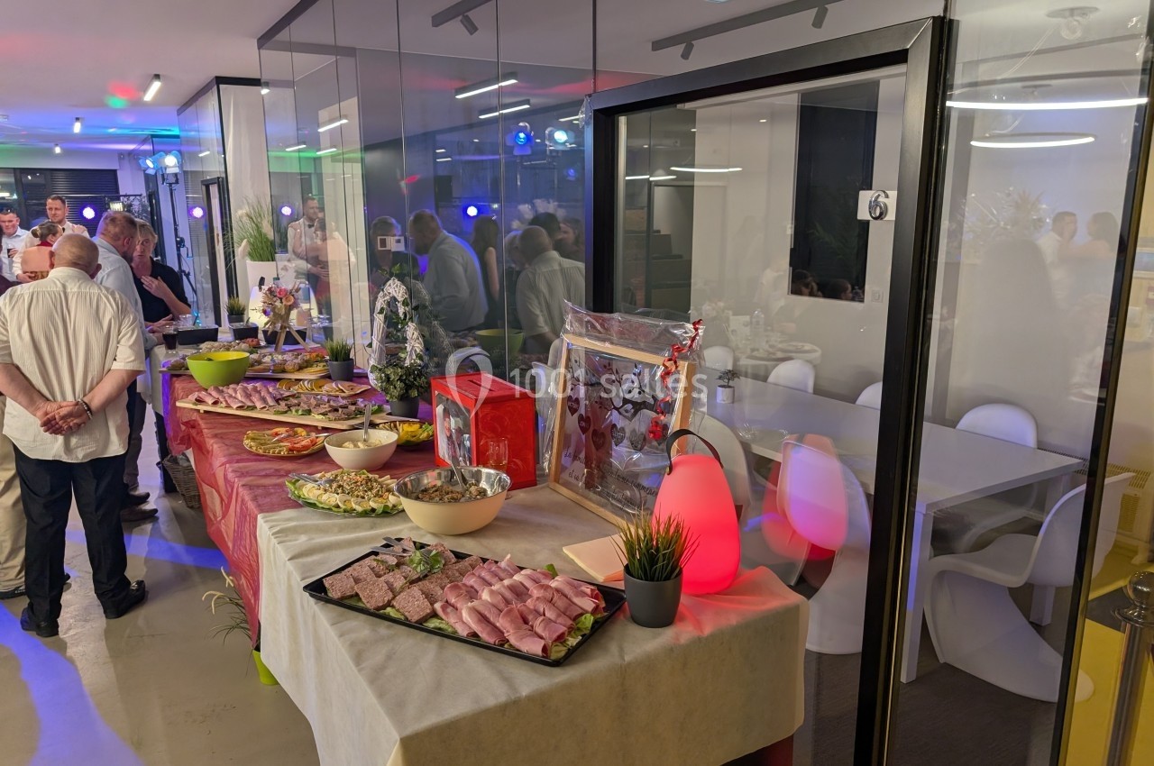 Buffet avec charcuterie, salades et décorations, dans une salle lumineuse avec des invités en arrière-plan.