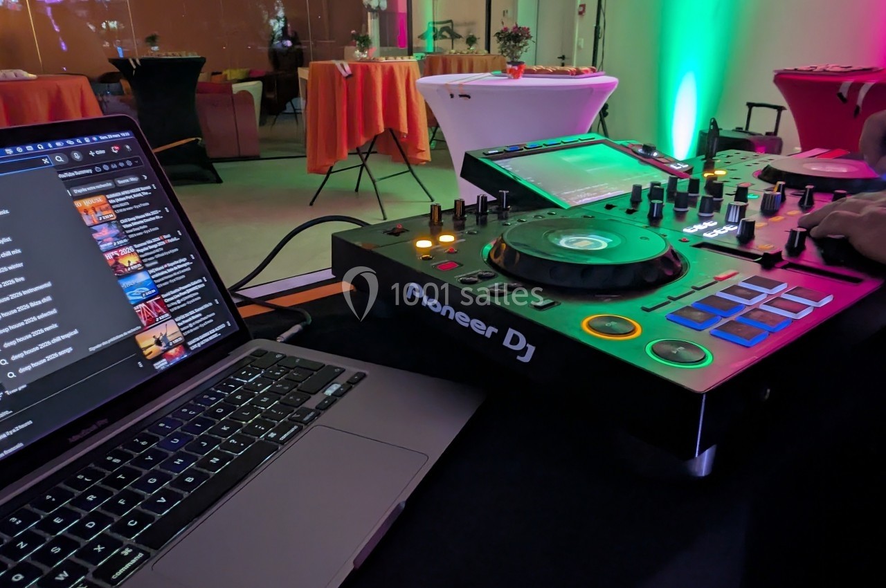 Table de mixage Pioneer DJ et ordinateur portable sur une table dans une salle éclairée par des lumières colorées.