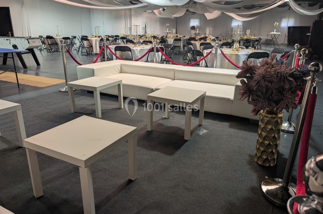 Espace lounge avec canapés blancs, tables basses et décorations dans une salle de réception élégamment aménagée.