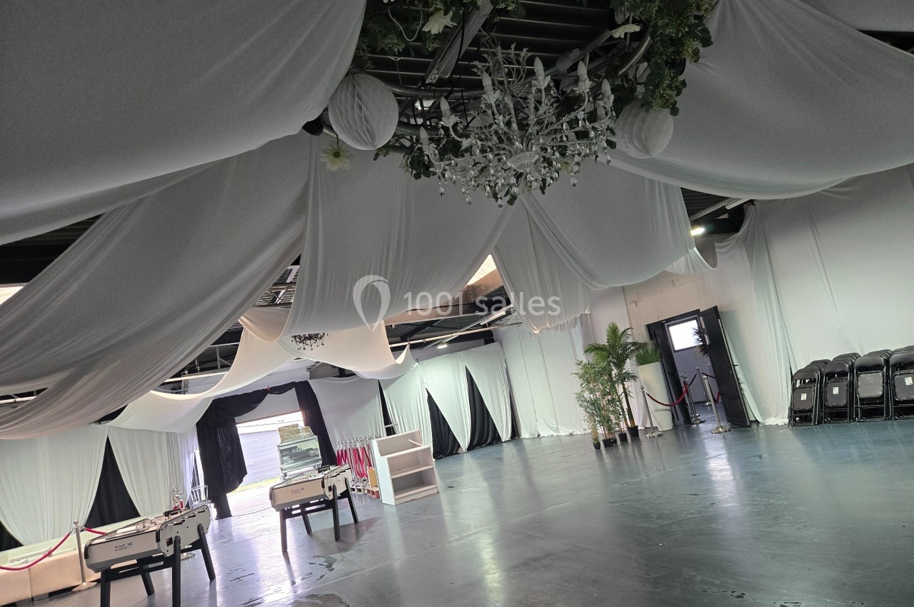 Salle décorée de drapés blancs suspendus au plafond, avec des baby-foot et des plantes en arrière-plan.