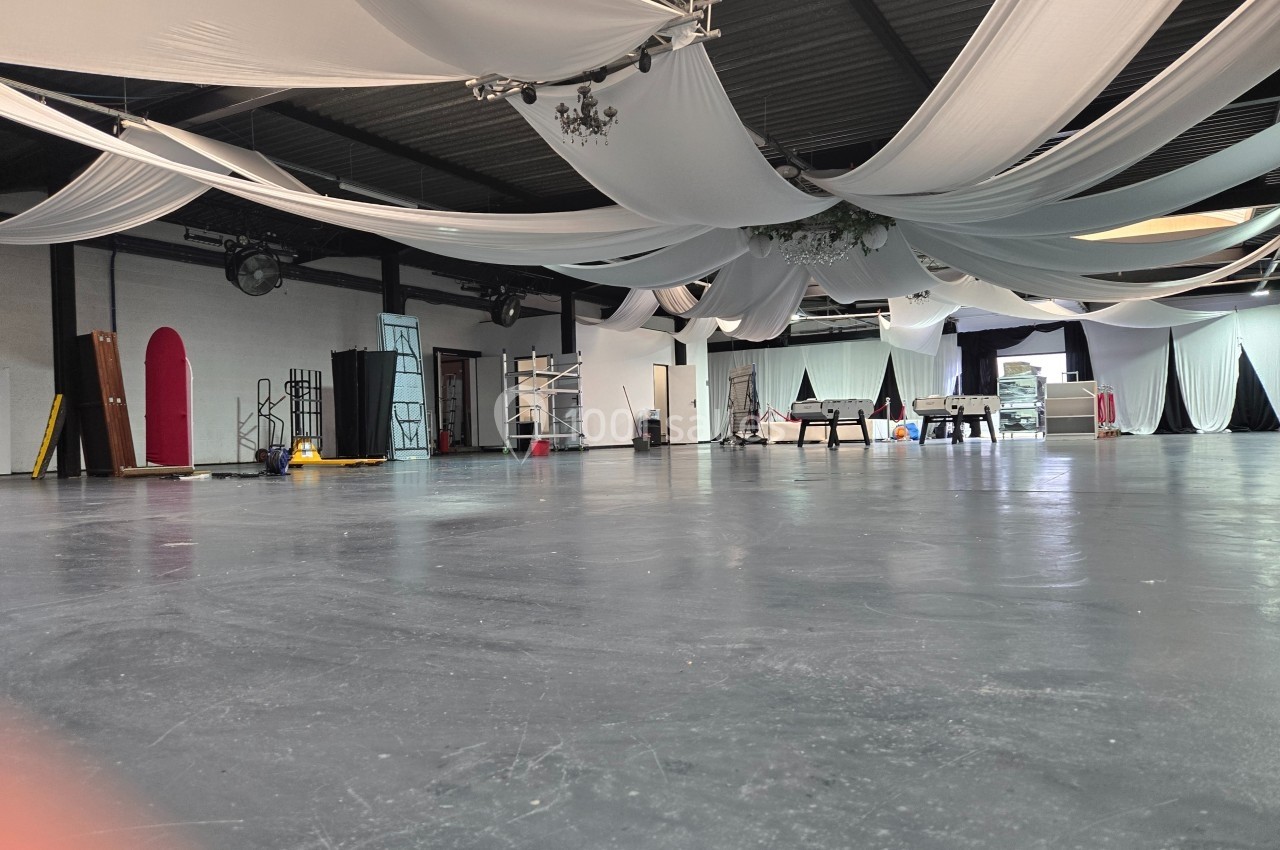 Grande salle avec un sol gris, des drapés blancs suspendus au plafond et divers équipements disposés autour.