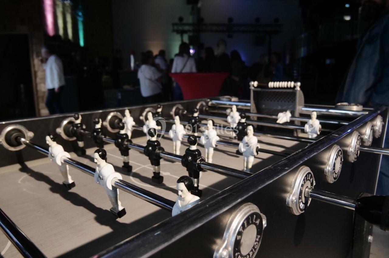 Vue rapprochée d'un baby-foot dans un espace intérieur avec des silhouettes de personnes en arrière-plan.