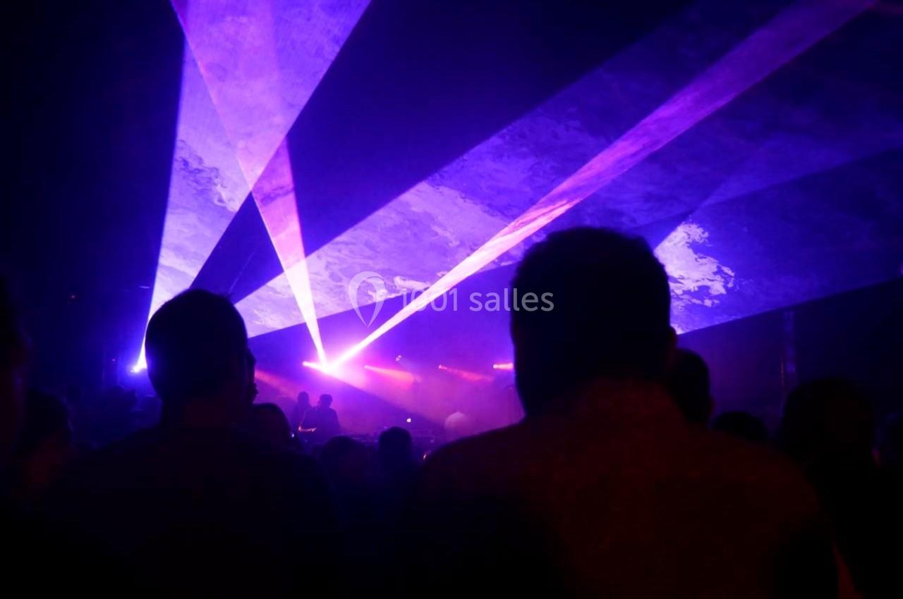Silhouettes de personnes dans une salle sombre avec des faisceaux lumineux violets et bleus traversant la scène.