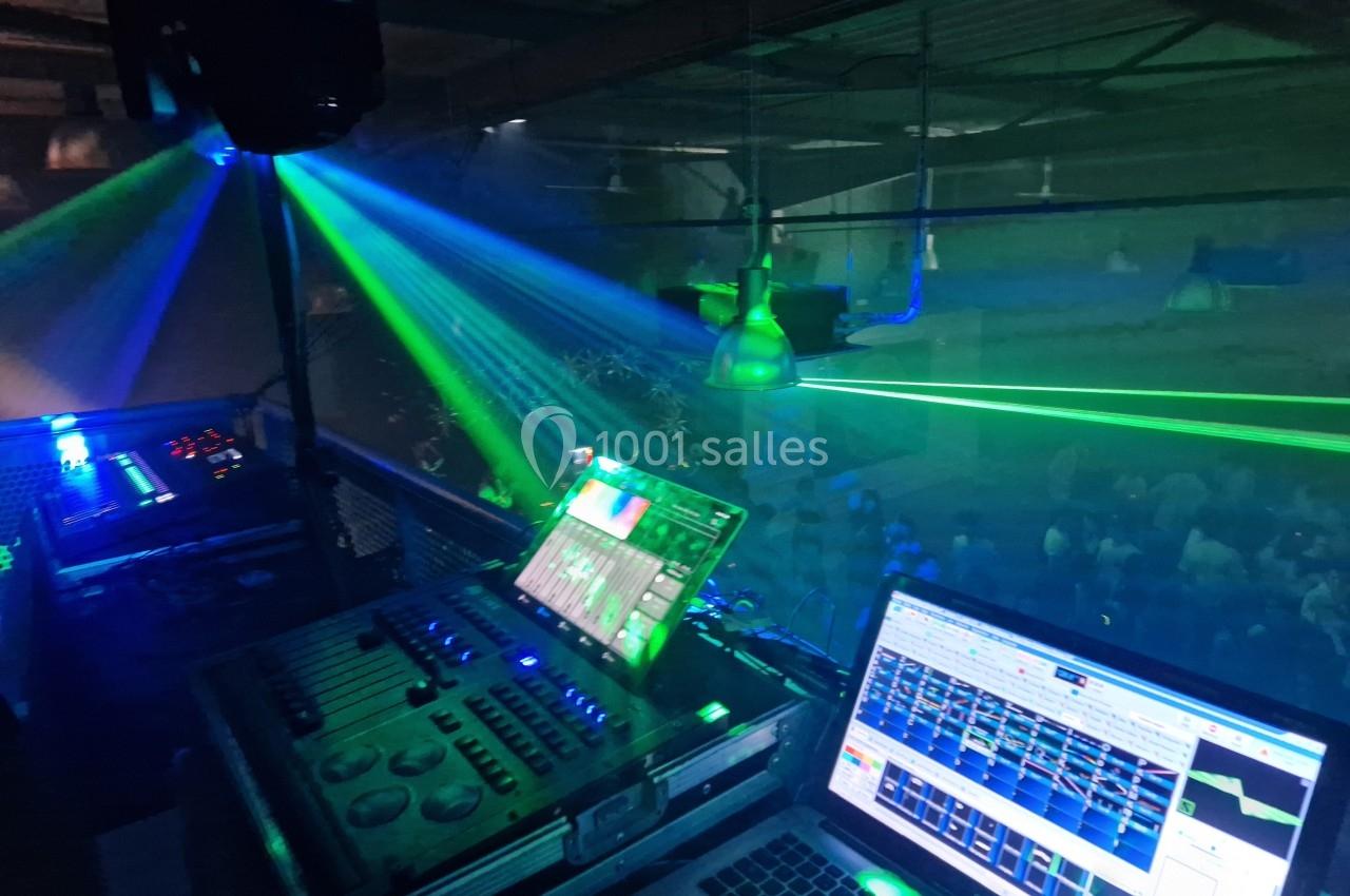 Poste de contrôle lumineux avec consoles et ordinateurs, diffusant des faisceaux laser colorés dans une salle sombre.