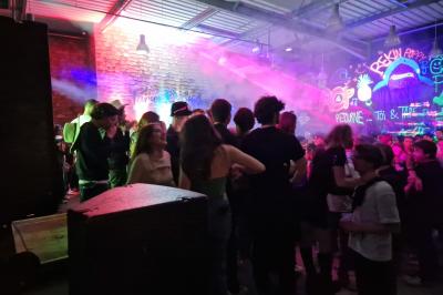 Un grand groupe de jeunes assis dehors sur un sol en béton, près de bâtiments sous un ciel nuageux.
