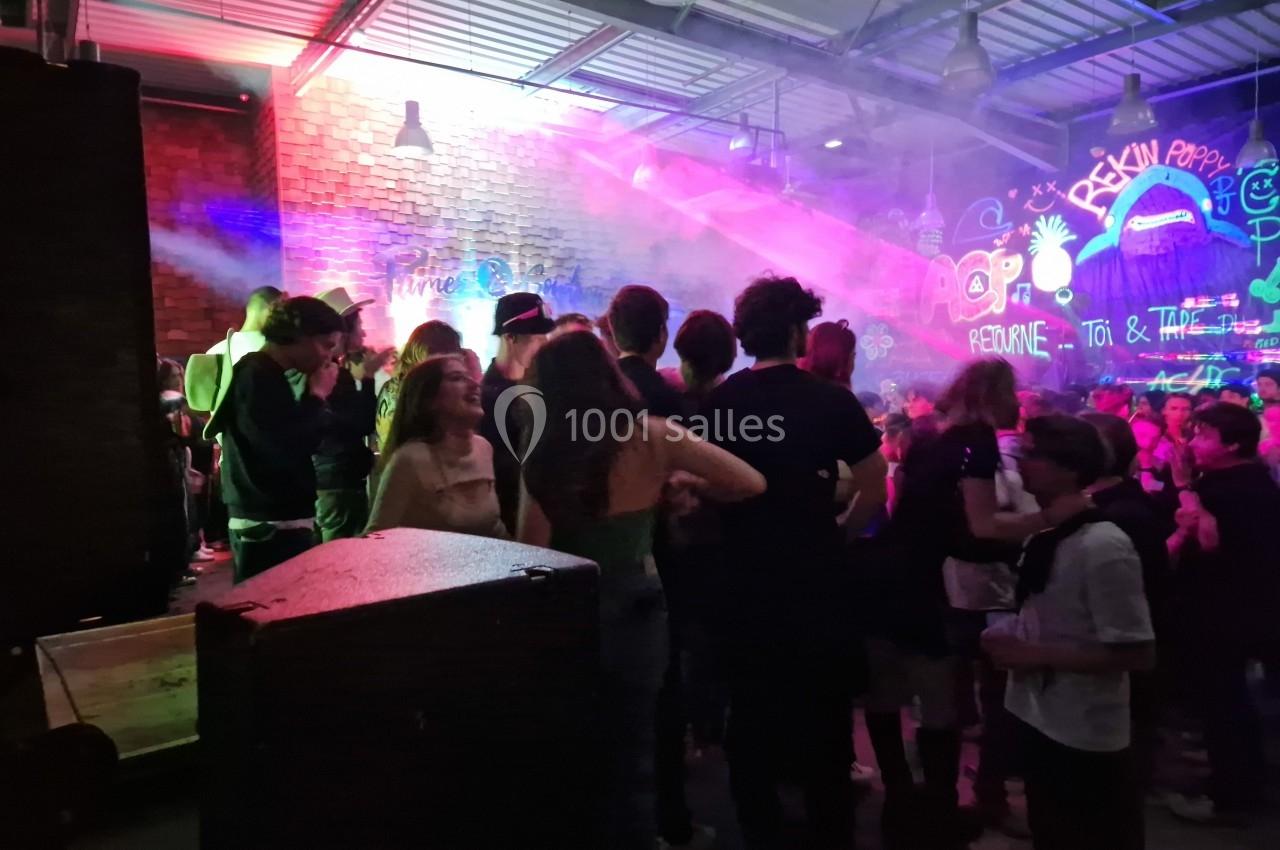 Groupe de personnes debout dans une salle animée avec des jeux de lumière et des graffitis colorés sur les murs.