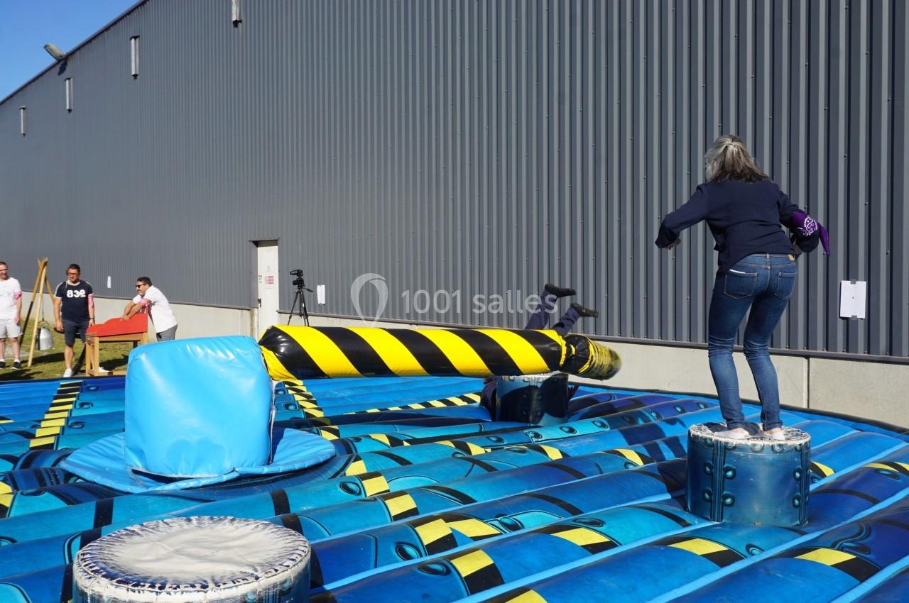 Personnes participant à un jeu gonflable où elles évitent une barre rotative dans un espace extérieur.