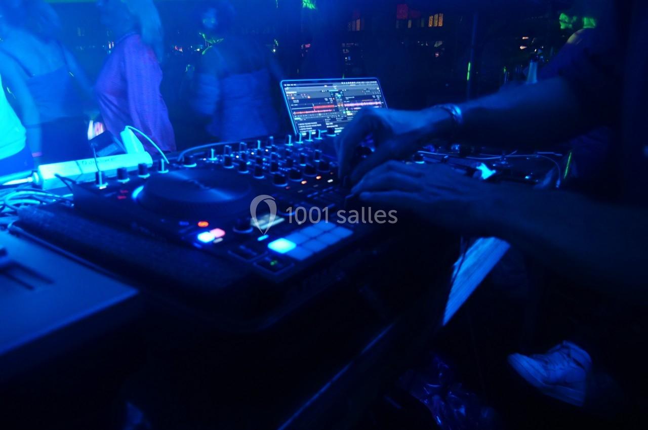 Un DJ mixe de la musique sur une table de mixage éclairée dans une ambiance de boîte de nuit sombre.