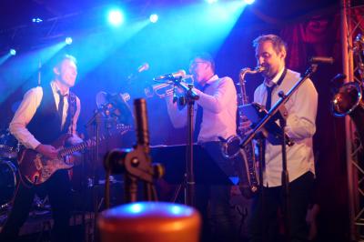Un grand groupe de jeunes assis dehors sur un sol en béton, près de bâtiments sous un ciel nuageux.