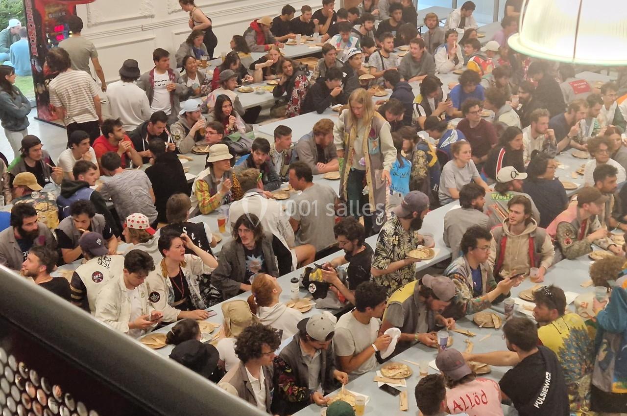 Un grand groupe de personnes assises à des tables, partageant un repas dans une salle animée.