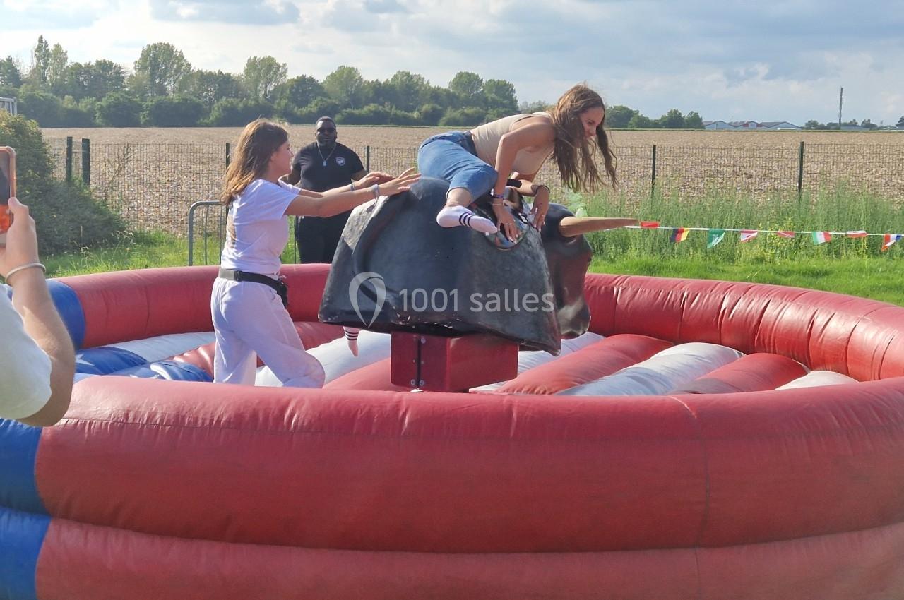 Deux personnes participent à une activité de rodéo mécanique en plein air, entourées d'un champ et de spectateurs.