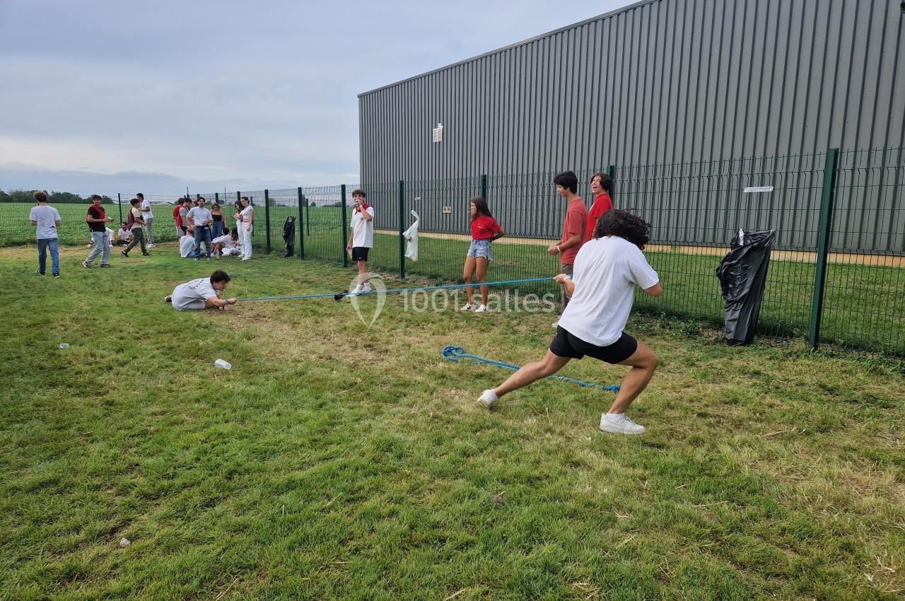 Des personnes participent à un jeu de tir à la corde sur une pelouse près d'un bâtiment en métal.