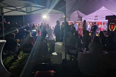 Un grand groupe de jeunes assis dehors sur un sol en béton, près de bâtiments sous un ciel nuageux.