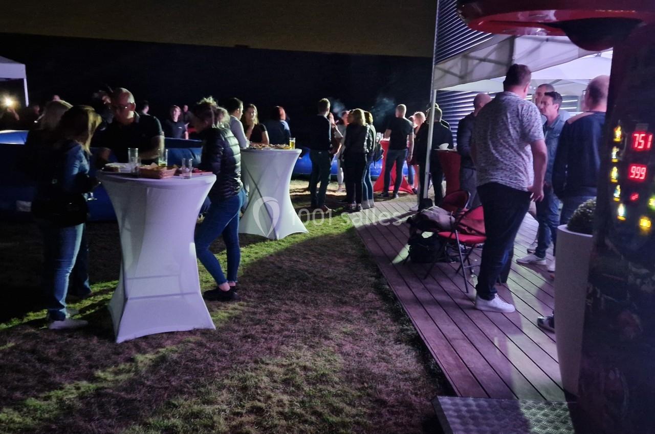 Groupe de personnes discutant et mangeant autour de tables hautes lors d'un événement en extérieur, de nuit.
