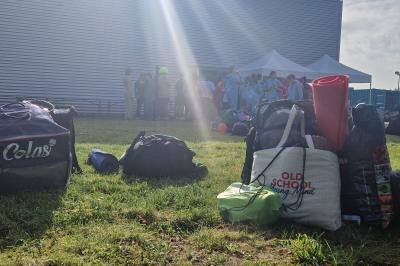 Un grand groupe de jeunes assis dehors sur un sol en béton, près de bâtiments sous un ciel nuageux.