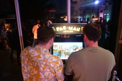 Un grand groupe de jeunes assis dehors sur un sol en béton, près de bâtiments sous un ciel nuageux.