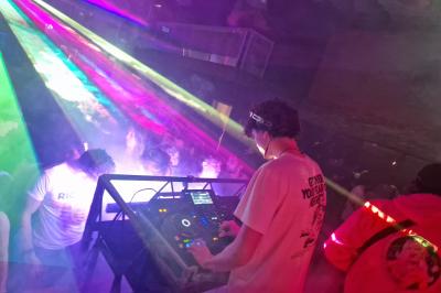 Un grand groupe de jeunes assis dehors sur un sol en béton, près de bâtiments sous un ciel nuageux.