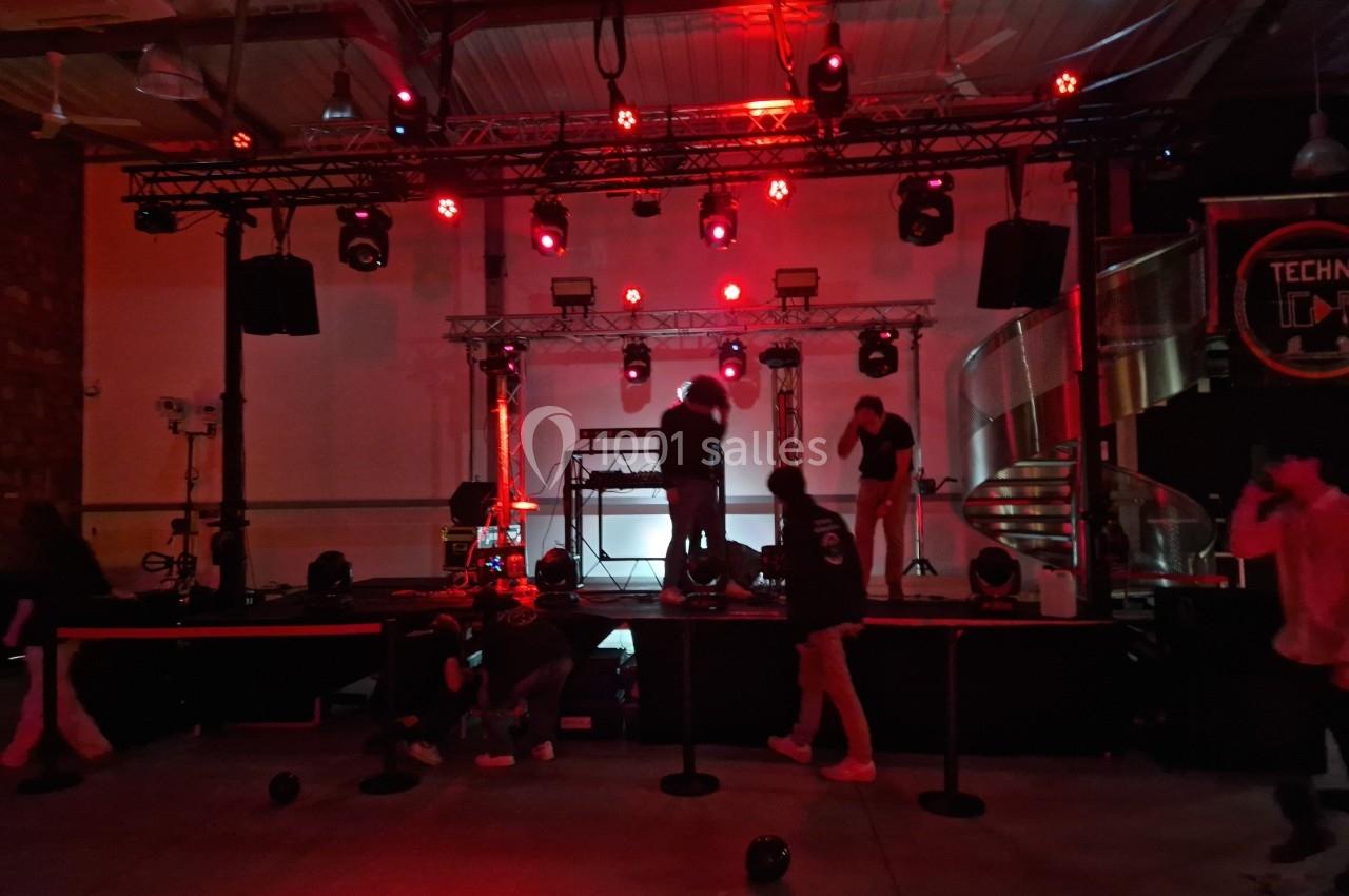 Scène de concert en préparation avec des techniciens ajustant l'éclairage rouge dans une salle sombre.