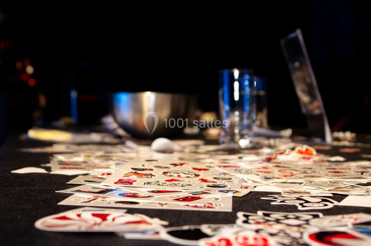 Cartes colorées éparpillées sur une table sombre avec un bol métallique et des verres en arrière-plan.
