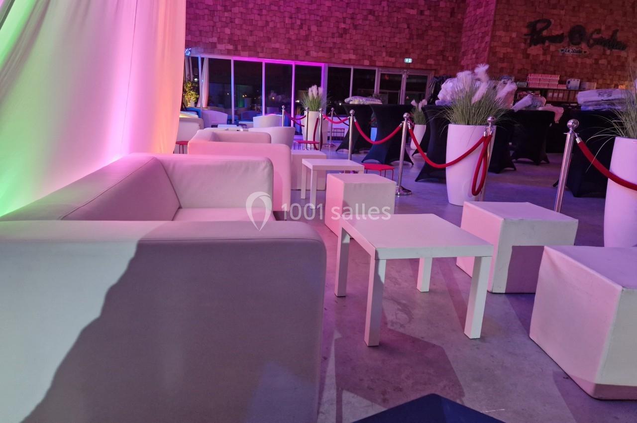 Espace lounge avec canapés blancs, tables basses et éclairage coloré dans une salle à la décoration moderne.