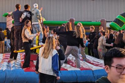 Un grand groupe de jeunes assis dehors sur un sol en béton, près de bâtiments sous un ciel nuageux.