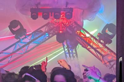 Un grand groupe de jeunes assis dehors sur un sol en béton, près de bâtiments sous un ciel nuageux.