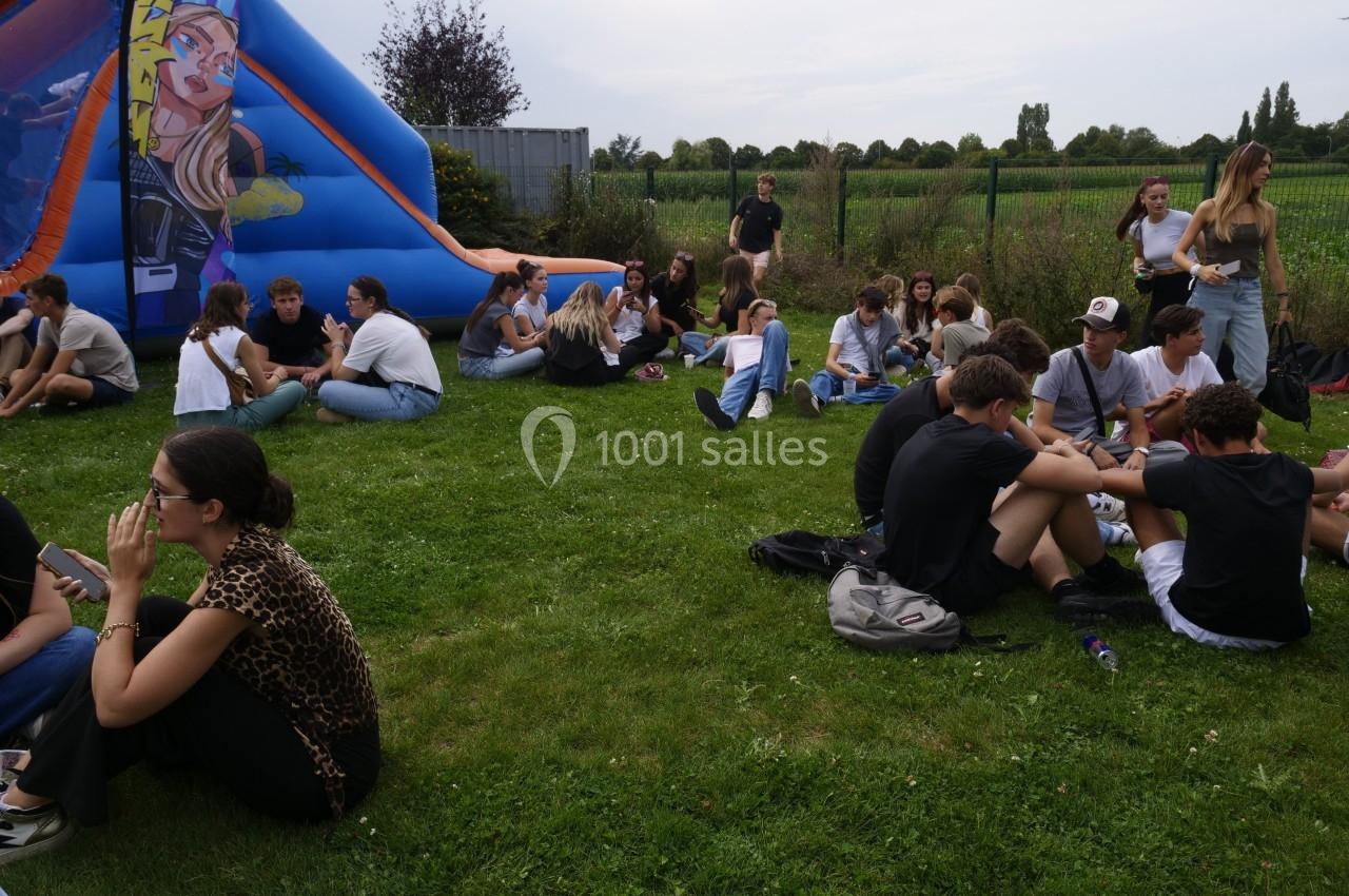 Des personnes assises sur une pelouse discutent par petits groupes près d'une structure gonflable colorée en extérieur.