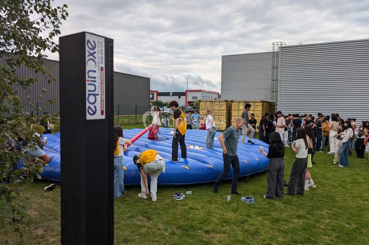 Des personnes participent à une activité sur une structure gonflable dans un espace extérieur, entourées de bâtiments.