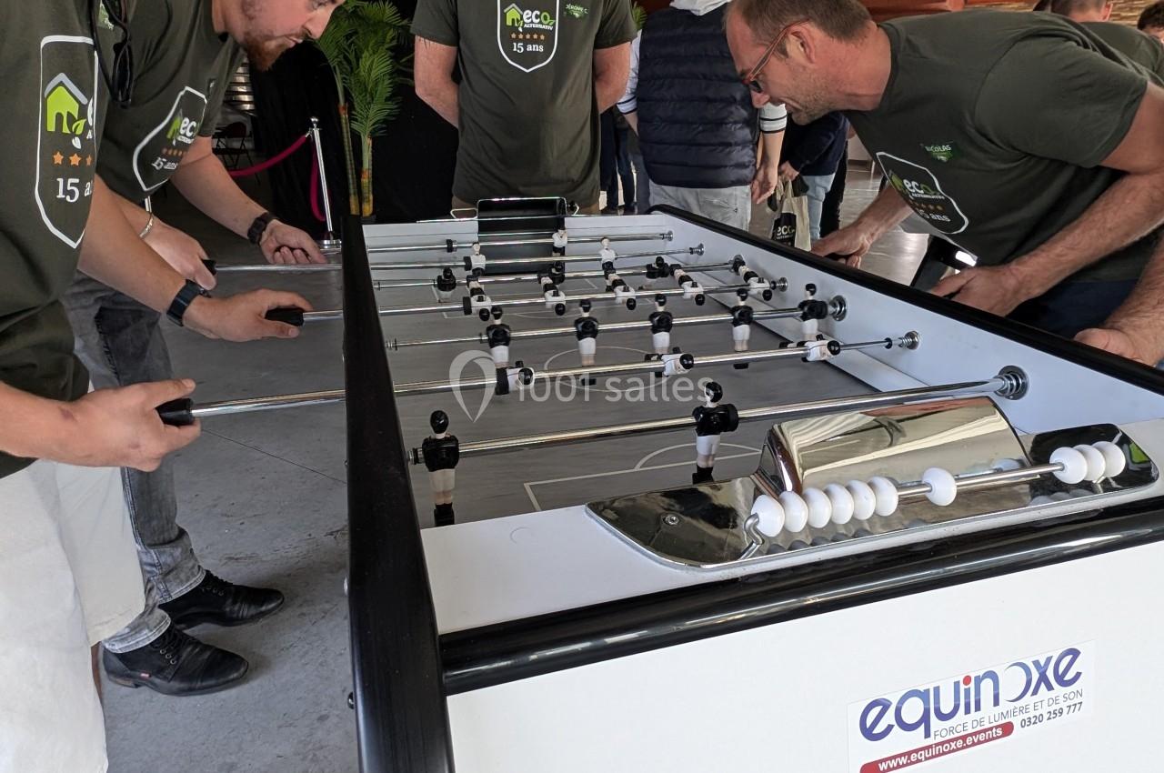 Des personnes jouent au baby-foot sur une table blanche dans un espace intérieur.