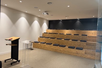 Un grand groupe de jeunes assis dehors sur un sol en béton, près de bâtiments sous un ciel nuageux.