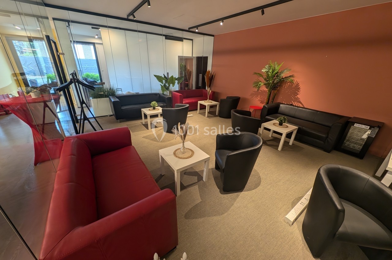 Salle d'attente moderne avec canapés rouges et noirs, tables basses blanches et plantes décoratives.