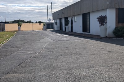 Un grand groupe de jeunes assis dehors sur un sol en béton, près de bâtiments sous un ciel nuageux.