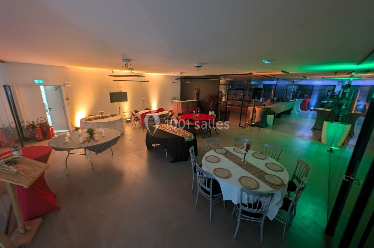 Salle aménagée pour un événement, avec tables rondes dressées, éclairage tamisé et décorations simples.