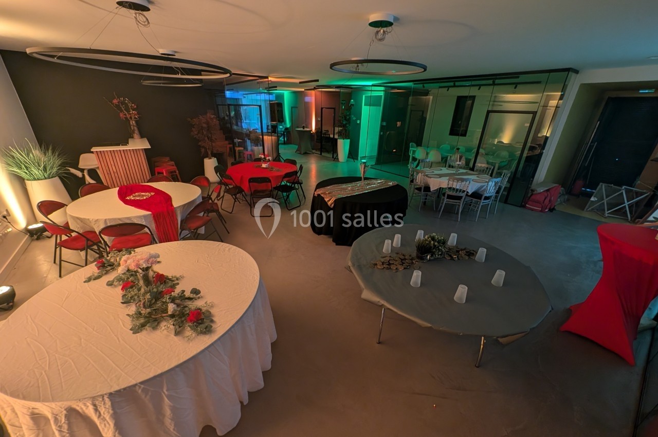 Salle décorée pour un événement avec des tables rondes recouvertes de nappes, éclairage tamisé et ambiance chaleureuse.