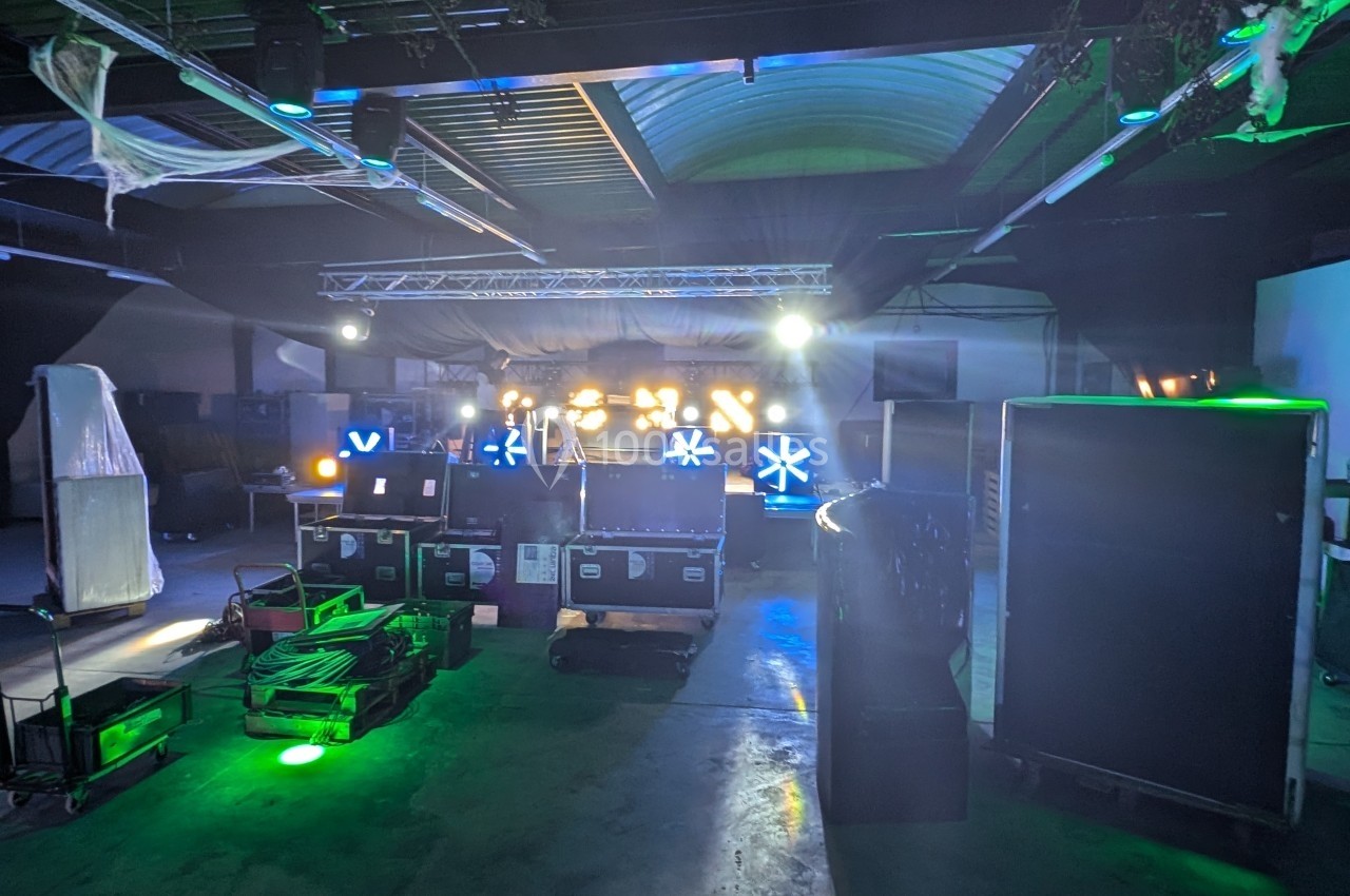 Salle sombre avec équipements de scène, projecteurs allumés et effets lumineux colorés en arrière-plan.