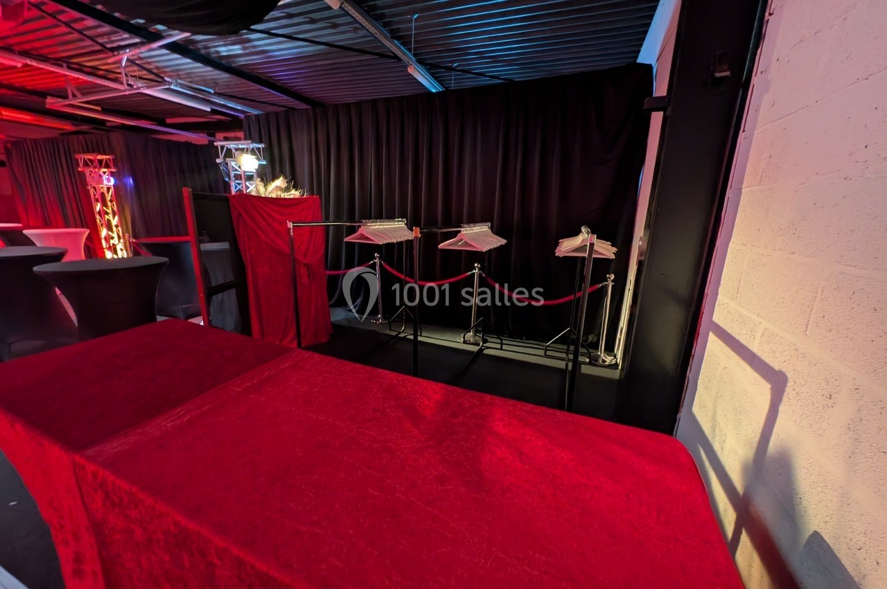 Portant avec cintres vides derrière une barrière rouge, dans une salle éclairée par des lumières tamisées.