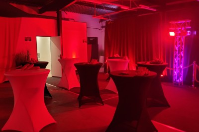 Des enfants colorient des dessins autour d'une table ronde, entourés d'adultes dans un espace intérieur animé.