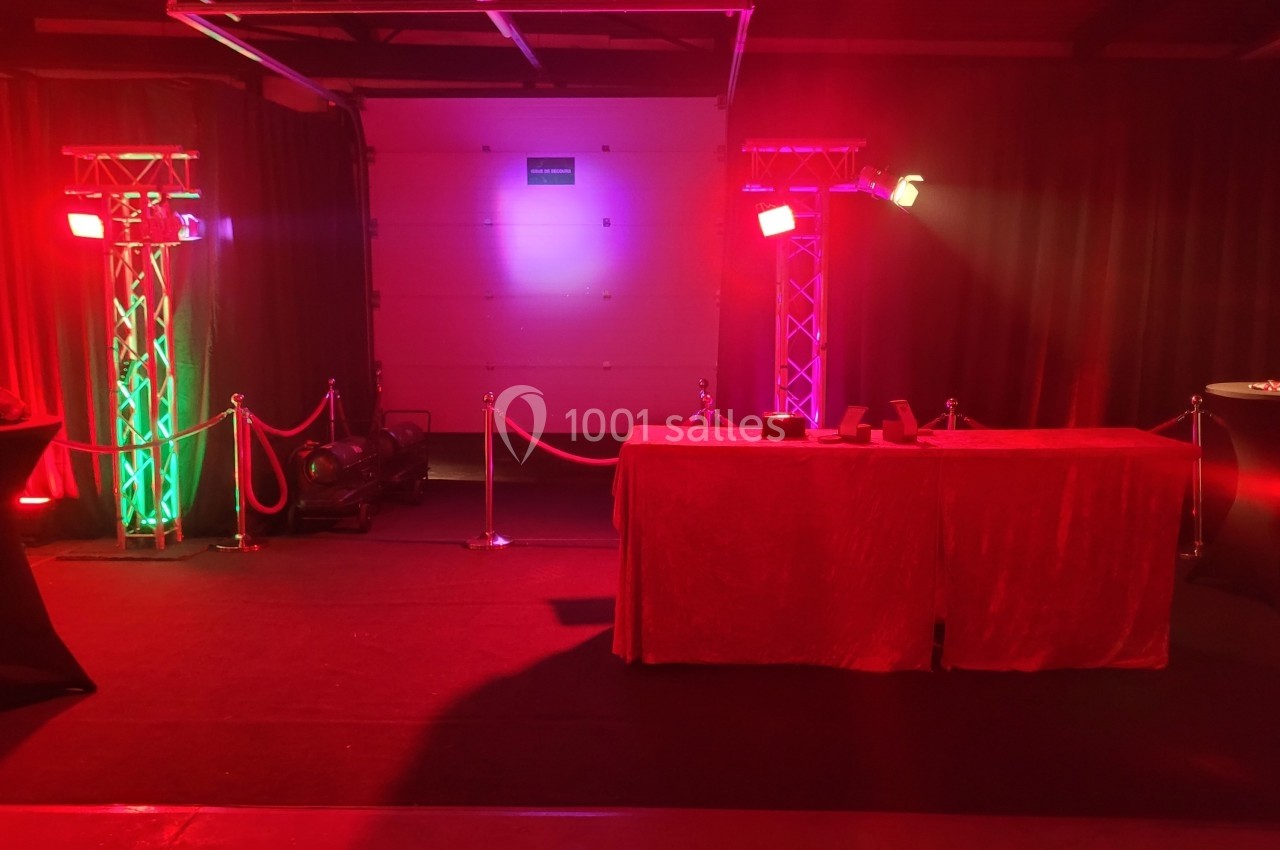 Table recouverte d'une nappe rouge entourée de poteaux avec cordons, éclairée par des lumières rouges et vertes.