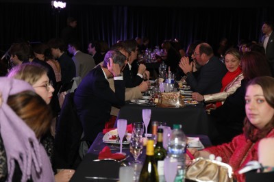 Des enfants colorient des dessins autour d'une table ronde, entourés d'adultes dans un espace intérieur animé.