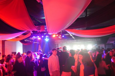 Des enfants colorient des dessins autour d'une table ronde, entourés d'adultes dans un espace intérieur animé.