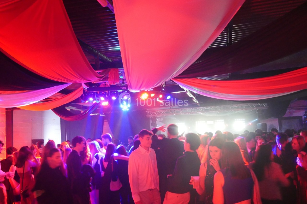 Salle de fête animée avec des personnes dansant sous des éclairages colorés et des drapés suspendus au plafond.