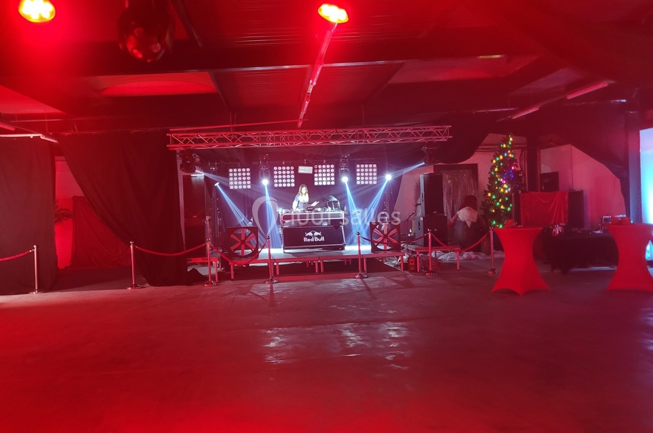 Salle de réception avec éclairage rouge, scène centrale équipée d'un DJ et d'un équipement sonore, décorations festives en…